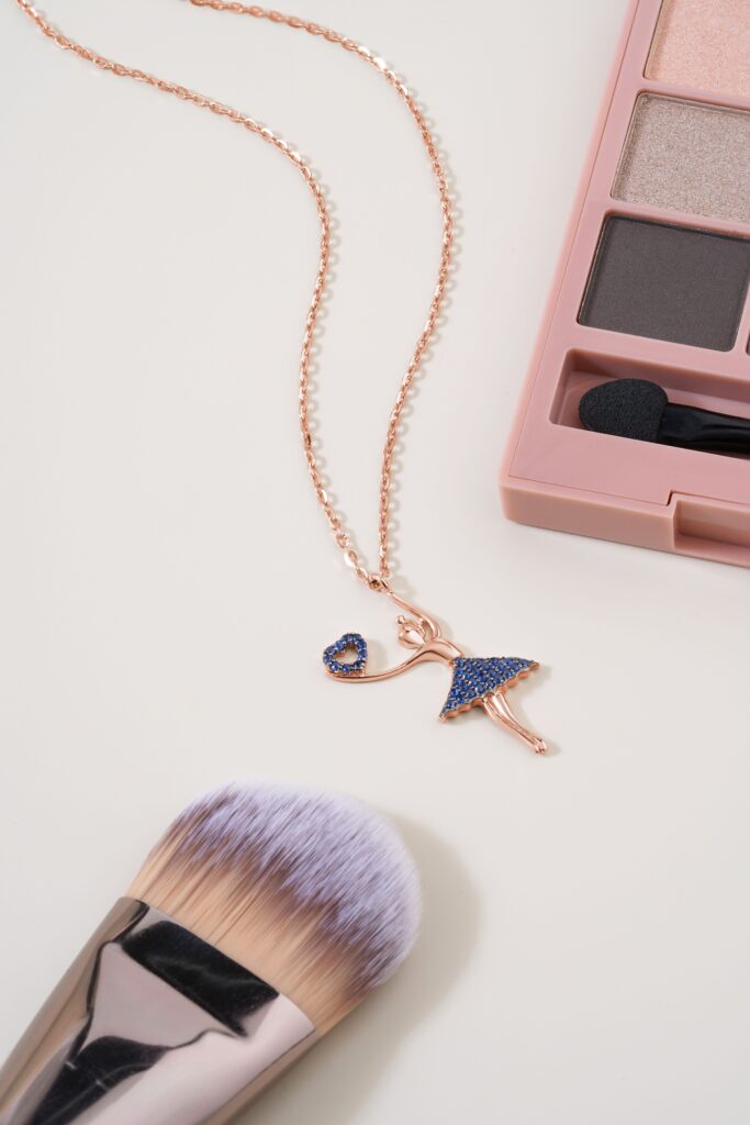 Close-up of a delicate necklace with a ballet dress pendant, surrounded by makeup items.